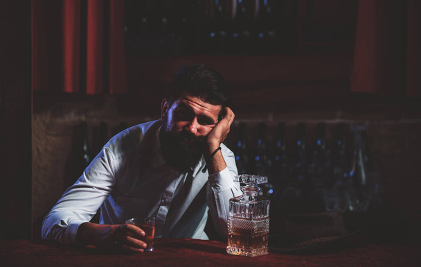 Drunk man sitting at the counter in a pub or a bar and drinking cognac or whiskey. Scotch and cognac. - 写真・画像