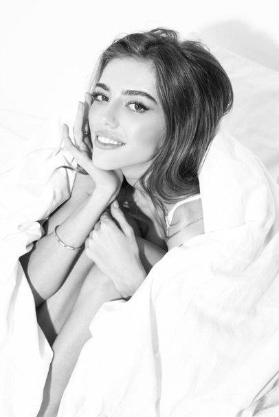 Sensual woman wrapped in soft blanket sitting on bed. Sexy woman sitting in bed and smiling at home. - Foto, afbeelding