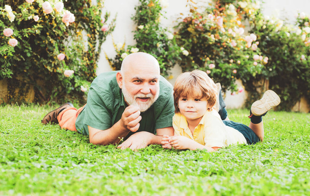 Senior man with grandson jogging in park. Cute child boy hugging his grandfather. Healthcare family lifestyle. Happy grandfather and grandson relaxing together. - Zdjęcie, obraz