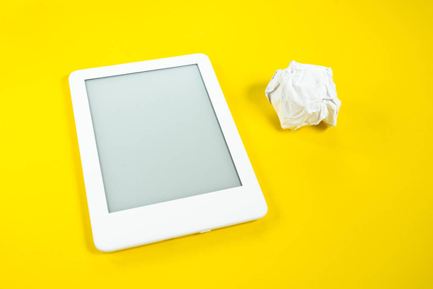 Ebook lezer over gele achtergrond met papieren bal naast - Foto, afbeelding