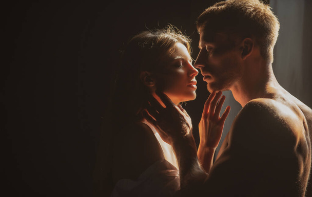 Romantic couple in love looking at each other, embracing and kissing on black background. Beautiful loving couple posing on dark backgroung with night lights. - Foto, Imagem