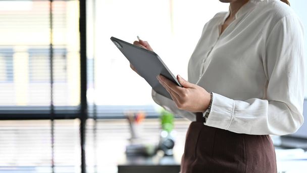 Mujer de negocios en traje formal de pie en la oficina y utilizando tableta digital touchpad. imagen recortada - Foto, imagen