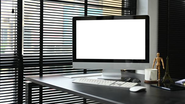 Egy PC számítógép fehér képernyős mockup egy modern sötét irodai asztalon az irodai szobában. Modern irodai munkaterület. - Fotó, kép