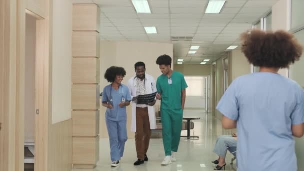 Group of practitioners team, Professional African American male doctor with medical students walk and discuss diagnosis X-ray film at international outpatient healthcare clinic in Thailand hospital. - Felvétel, videó