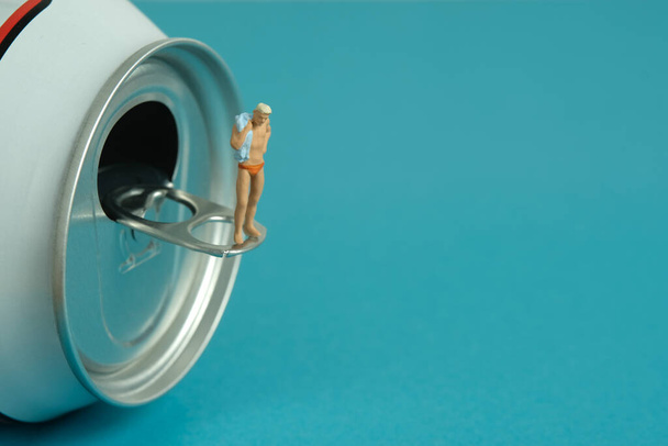 Miniature people toy figure photography. Creative summer vacation concept. A men standing above soft drink canned getting ready to swim. Image photo - Foto, immagini