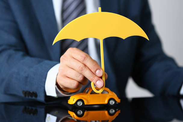 Férfi munkás öltönyben tartsa fa esernyő felett sárga autó modell, szimbóluma autóvédelem - Fotó, kép