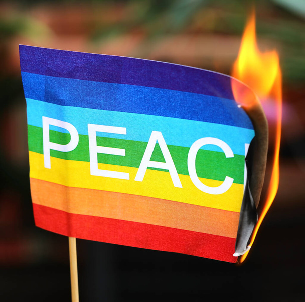 Σημαία ειρήνης με το κείμενο και τα χρώματα του ουράνιου τόξου καθώς πιάνει φωτιά συμβολίζοντας τον ατέλειωτο πόλεμο - Φωτογραφία, εικόνα