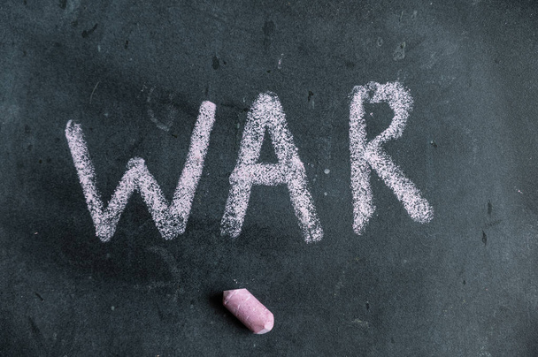 War. A word is written in pink chalk on a black chalkboard. Handwritten text. A piece of colored chalk hangs next to it. - 写真・画像