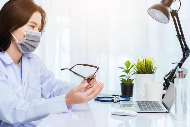 Asian young beautiful woman doctor wear face mask protective video call conference online raise hand explain to patients on laptop computer quarantines disease coronavirus or COVID-19 at hospital - 写真・画像