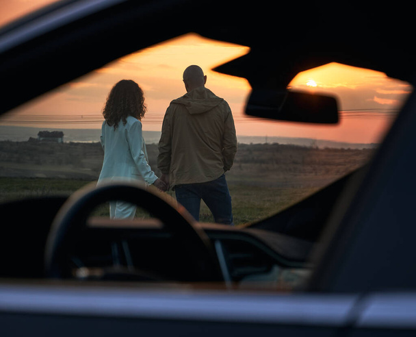 Couple romantique avec voiture profitant de l'atmosphère du soir au coucher du soleil. - Photo, image