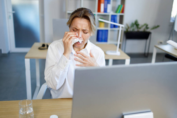 Donna d'affari sconvolta che piange nel fazzoletto mentre si siede sul posto di lavoro in ufficio - Foto, immagini