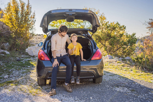Dad and son are resting on the side of the road on a road trip. Road trip with children concept - Photo, Image
