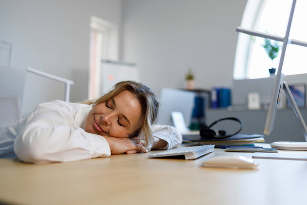 Een zakenvrouw van middelbare leeftijd die een dutje doet op het werk. Overwerkt vrouwelijk kantoorpersoneel - Foto, afbeelding