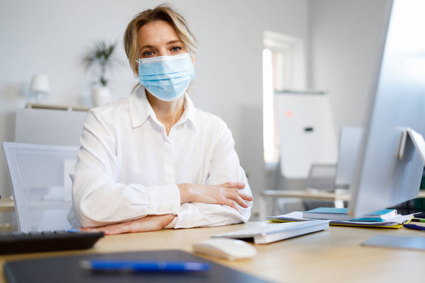 Vrouwelijke kantoormedewerker met een medisch masker - Foto, afbeelding
