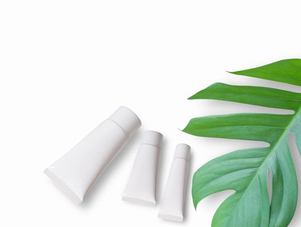 Widok z góry z białymi kosmetykami i zielonymi liśćmi na białym tle stołu. Naturalny produkt kosmetyczny do projektowania marki makiety koncepcja. - Zdjęcie, obraz