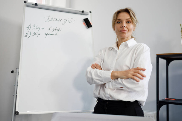 Retrato de mujer de negocios positiva en camisa blanca con brazos cruzados cerca del rotafolio magnético - Foto, imagen