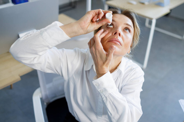 Business woman applying eye drops. Occupational disease concept - 写真・画像