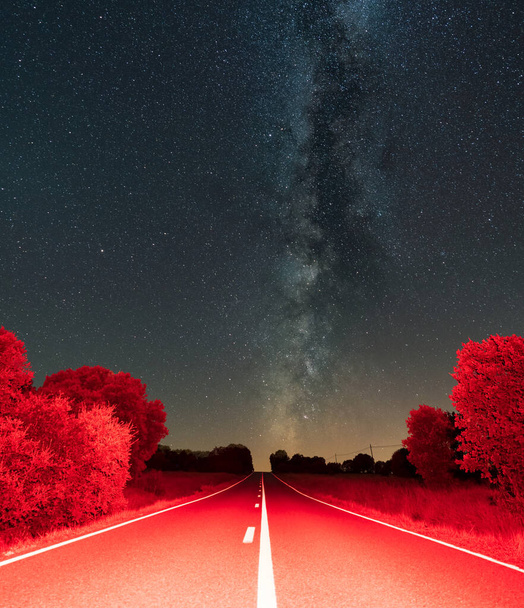 Straight red road with white lines under the milky way - 写真・画像