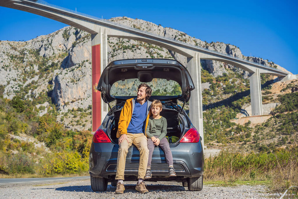 Montenegro. Dad and son tourists are sitting on the trunk of a car. Road trip around Montenegro. Bridge Moracica. Reinforced concrete bridge across the Moraci gorge. The motorway Bar - Bolyare. The - Photo, Image
