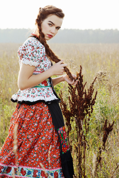 Young peasant woman, dressed in Hungarian national costume, posing over nature background - Photo, image