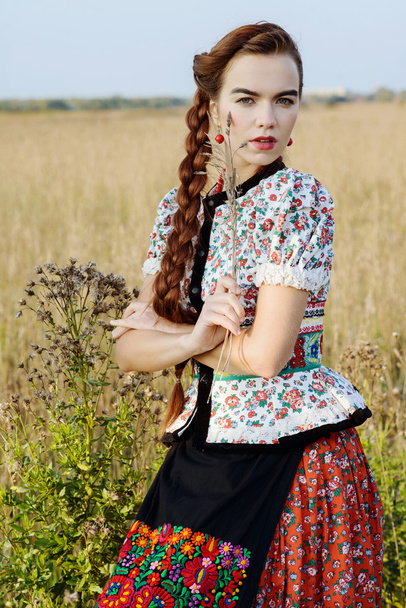 Young peasant woman, dressed in Hungarian national costume, posing over nature background - Foto, afbeelding