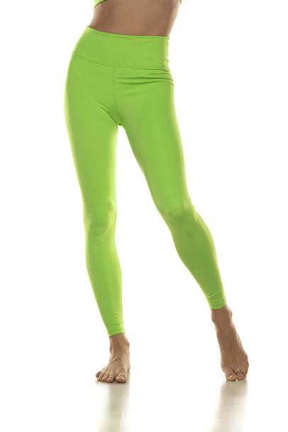 Urheilullinen vihreä leggingsit hoikka melko paljain jaloin valkoisella pohjalla. Etunäkymä. - Valokuva, kuva