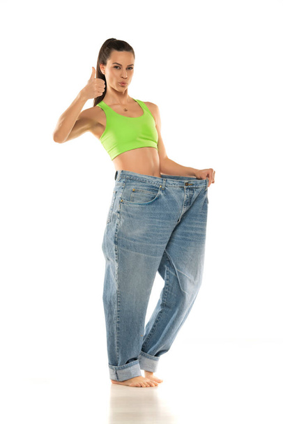 Diet concept and weight loss. Happy woman in oversize jeans on white background. - Fotó, kép