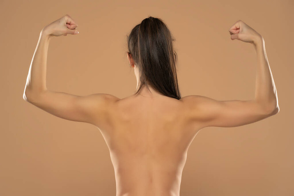 Back view of young nude woman with ponytail, showing arms on a beige background. - Fotoğraf, Görsel