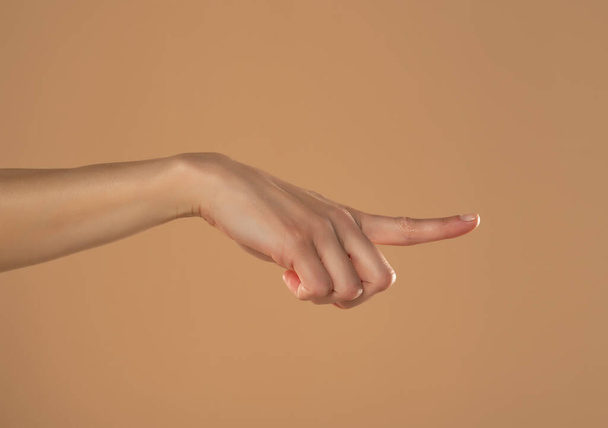 Young woman's palm touching imaginary product with index finger. Isolated on beige background. - Photo, image