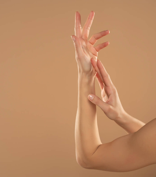 Ausschnittsaufnahme einer Frau, die Kosmetikprodukte auf ihre Hände auf beigem Hintergrund aufträgt. Junge Frau trägt Handcreme auf. - Foto, Bild