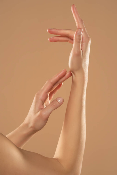 Foto recortada de mujer que aplica producto cosmético en sus manos sobre un fondo beige. Mujer joven aplicando crema de manos. - Foto, Imagen