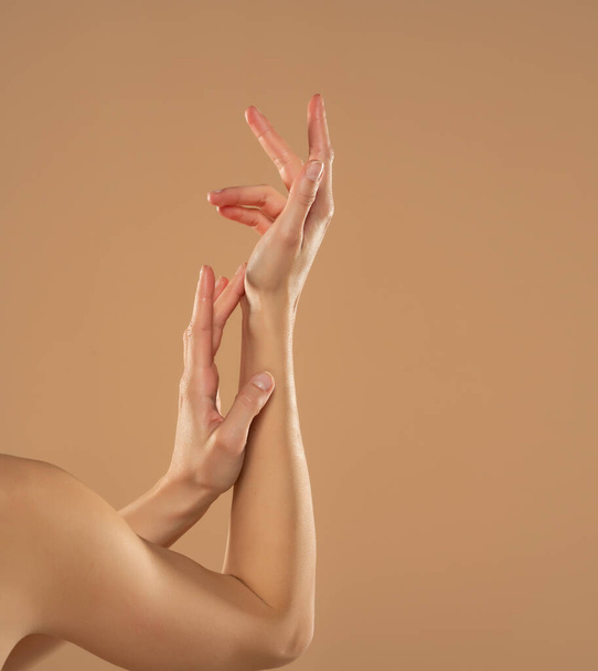 Cropped shot of woman applying cosmetic product on her hands on a beige background. Young woman applying hand cream. - Foto, Imagen