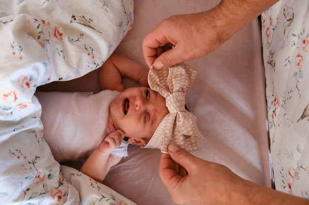 De handen van een zorgzame vader leggen een pasgeboren baby in een babybed met een strik. Top view, close-up, selectieve focus. - Foto, afbeelding