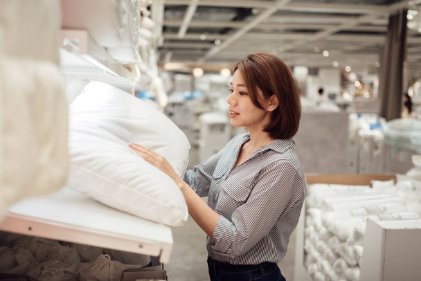 An Asian woman is choosing a pillow at the mall. - Zdjęcie, obraz