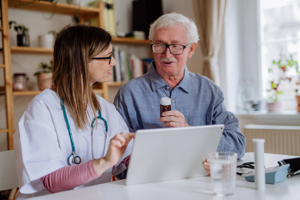 Healthcare worker or caregiver visiting senior man indoors at home, explaining medicine dosage. - Foto, immagini