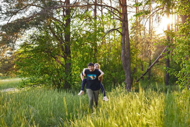 Father giving piggyback ride to small daughter on a walk in summer forest. - Valokuva, kuva