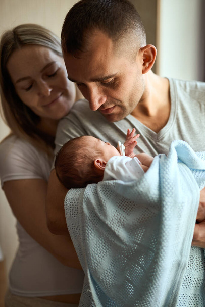 Mujer y hombre sosteniendo a un recién nacido. Mamá, papá y bebé. Primer plano. Retrato de familia joven sonriente con recién nacido en las manos. - Foto, Imagen