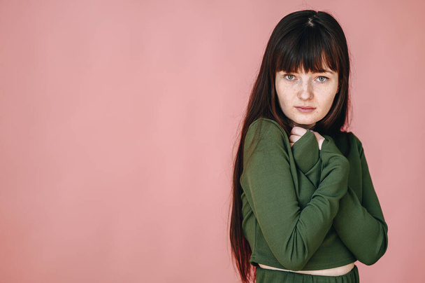 A young girl on a pink background stands in a closed pose with her arms crossed over her chest and looks at the camera. Defenselessness concept - Foto, imagen