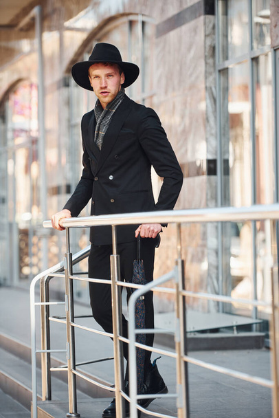 Elegant young man in black hat and with umbrella outdoors in the city. - Foto, Imagen