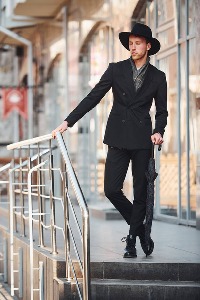 Elegant young man in black hat and with umbrella outdoors in the city. - 写真・画像