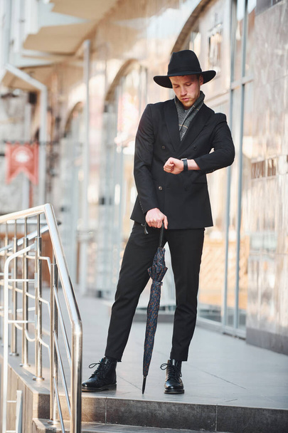 Elegant young man in black hat and with umbrella outdoors in the city. - Photo, image