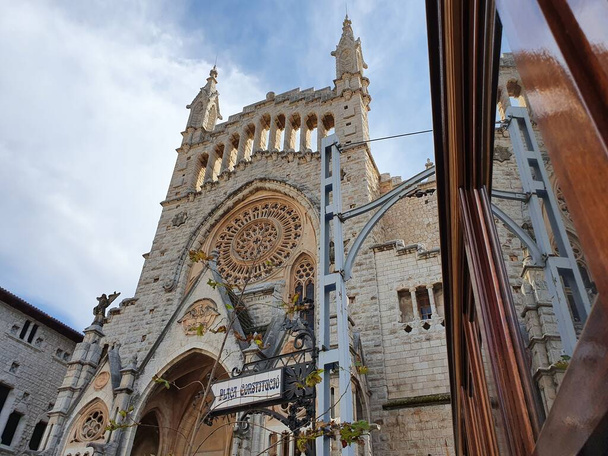 Die modernistische Fassade der Pfarrkirche von Sant Bartomeu, Soller, Mallorca, Balearen, Spanien, spiegelt sich im Fenster der Straßenbahn von Soller - Foto, Bild