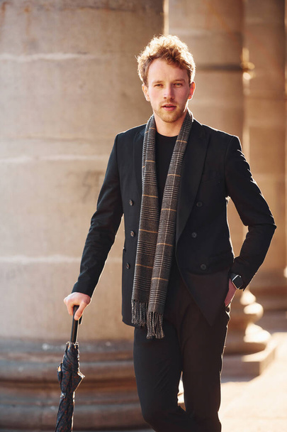 Holding umbrella. Elegant young man in formal classy clothes outdoors in the city. - Zdjęcie, obraz