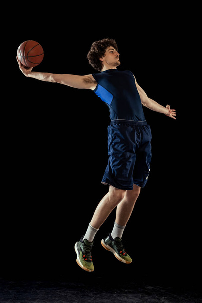 Professional basketball player in action and motion isolated on dark background. Concept of sport, competition, achievements, game. - 写真・画像