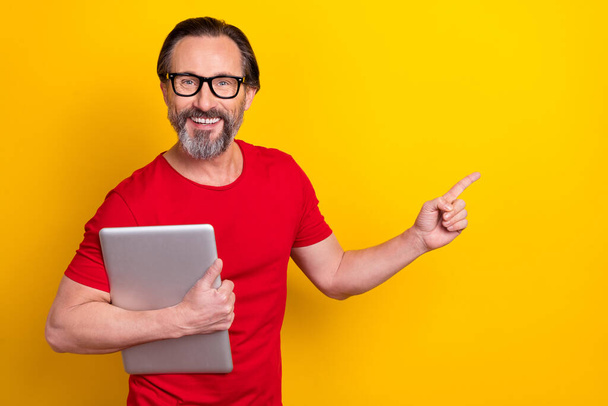 Photo of cheerful funny retired man wear red t-shirt spectacles holding modern device empty space isolated yellow color background - Valokuva, kuva