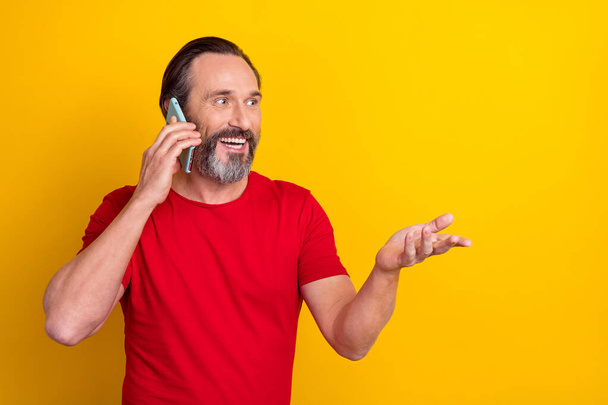 Foto van grappige volwassen brunet man zeggen telefoon dragen rood t-shirt geïsoleerd op gele kleur achtergrond - Foto, afbeelding