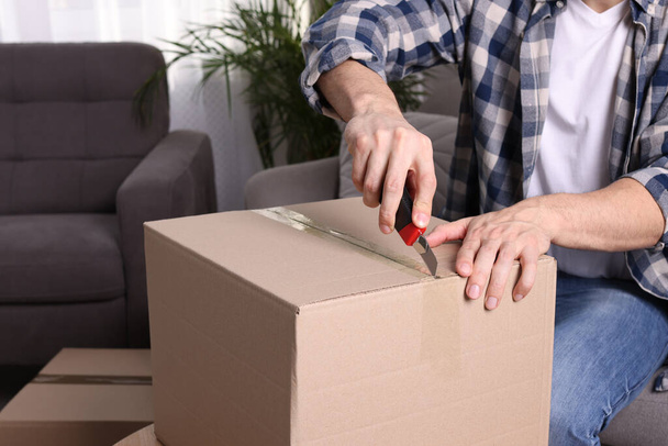 Man using utility knife to open parcel at home, closeup - Zdjęcie, obraz