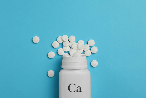 Overturned bottle of calcium supplement pills on light blue background, flat lay - Foto, afbeelding