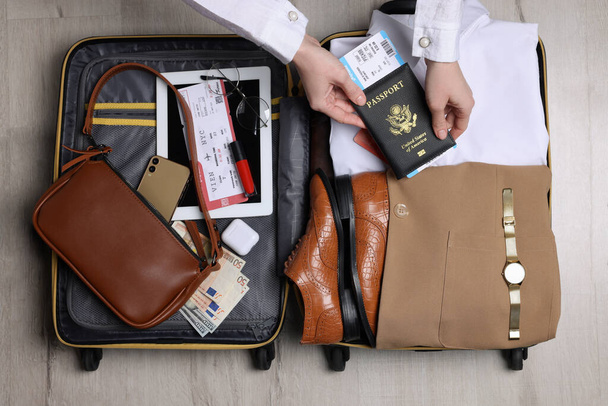 Woman packing suitcase for business trip on wooden floor, top view - Foto, imagen