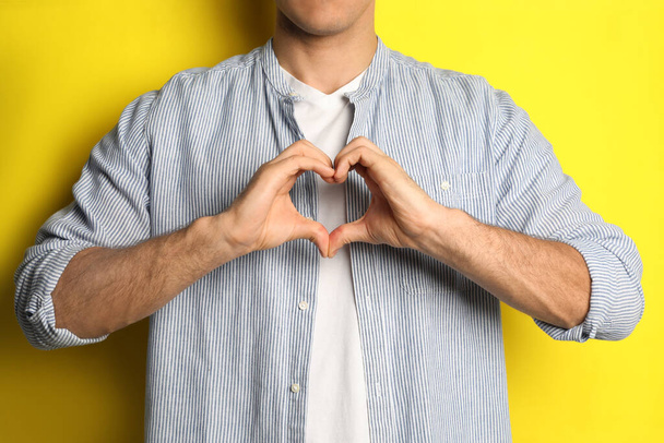 Uomo che fa il cuore con le mani su sfondo giallo, primo piano - Foto, immagini